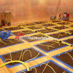 Yellow hoses and floor panels across a wood-floored room