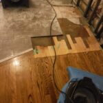 Lifted wood flooring beside an exposed base and blue air mover.