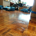 Air movers and blue drying equipment around a parquet floor.