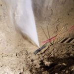 Water spraying onto soil beside a ladder and pink hose.
