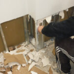 Restoration worker clearing broken plaster from an open wall.