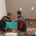 Restoration workers removing lower wall panels beside exposed studs.