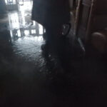 Worker's legs in a dim room with water across the floor.