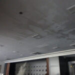 Ceiling with damaged areas and missing panels near large windows.