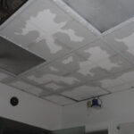 Ceiling panels with visible joint compound and an open panel space.