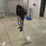 Restoration worker drawing an extraction wand across a tiled floor.