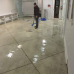 Restoration worker using a blue hose in a flooded commercial room.