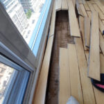 Loose wood planks and an open floor section beside tall windows.