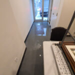 Standing water along a narrow hallway leading to a glass door.