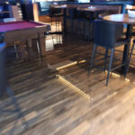 Water on a wood floor beside tall tables and a pool table.