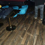Wet wood flooring beside blue chairs and black bar stools.