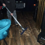 Restoration worker using an extraction wand beside blue chairs.