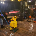 Restoration worker mopping a wet floor beside yellow buckets.
