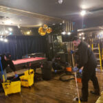 Restoration worker operating a hose beside a pool table.