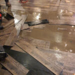 Lifted floorboards and standing water during indoor cleanup.