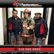 Three men in a hallway, one in firefighter gear and two in company jackets, posing for a photo with a contact number for emergency services visible, including flood restoration.