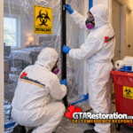 Technicians secure a plastic containment doorway marked with a biohazard warning sign.