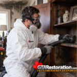 Technician wearing protective equipment vacuums soot from a wooden cabinet.