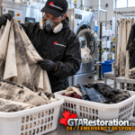 Technician examines soot-stained curtains beside laundry equipment and clothing baskets.
