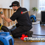 Technician checking exposed wood framing beside ducted drying equipment