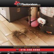 An image showing a leak from a water heater on a tiled floor with visible water damage and the logo and contact information for GTA Restoration, specializing in Water Damage Restoration.